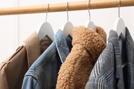 Different stylish clothes hanging on rack near white wall indoors, closeupの写真素材