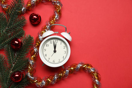 Alarm clock, fir tree branches, tinsel and baubles on red background, flat lay with space for text....