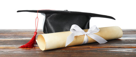Diploma and graduation hat on wooden table against white backgroundの写真素材