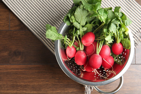 Fresh ripe radishes in colander on wooden table, top view. Space for text