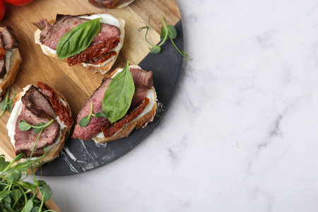 Bruschettas with roast beef, cream cheese, basil and sun-dried tomatoes on white marble table, top view. Space for textの写真素材