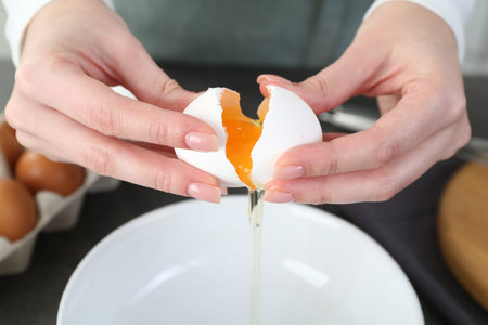 Woman cracking egg into bowl at gray table in kitchen, closeupの写真素材
