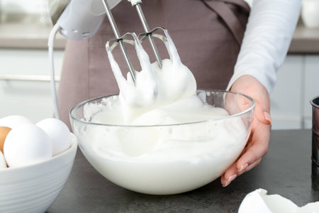 Woman beating egg whites with mixer at gray table in kitchen, closeupの写真素材