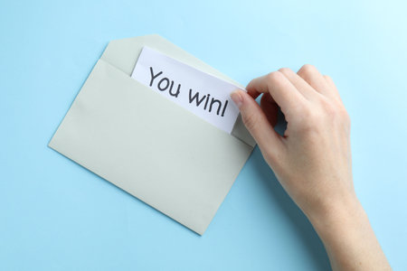 Woman taking card with text You Win! from envelope on light blue background, top viewの写真素材