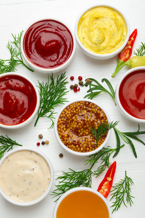 Different sauces in bowls and ingredients on white wooden table, flat layの写真素材