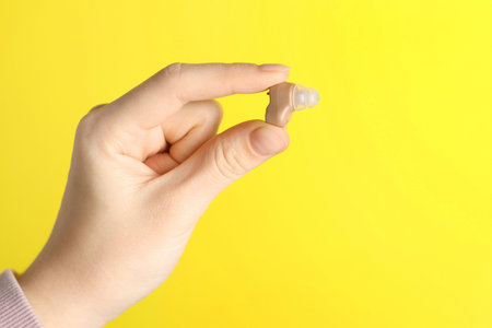 Woman with hearing aid on yellow background, closeup. Space for text