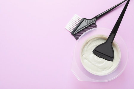 Hair dye in bowl and brushes on violet background, flat lay. Space for textの写真素材