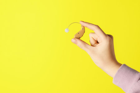 Woman with hearing aid on yellow background, closeup.の写真素材