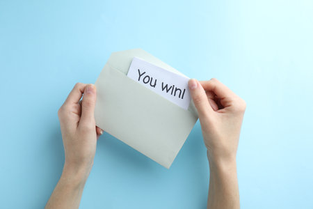 Woman taking card with text You Win! from envelope on light blue background, top viewの写真素材