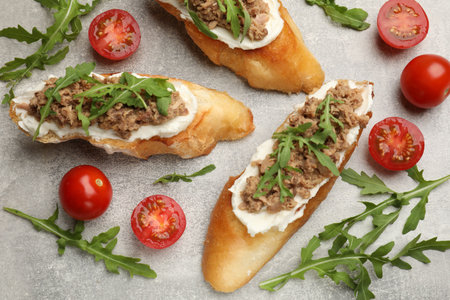 Delicious bruschettas with tuna, tomatoes and arugula on gray table, flat layの写真素材