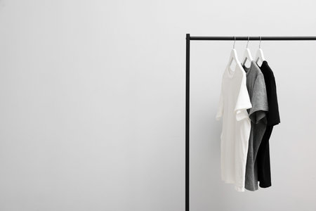 Different stylish t-shirts hanging on clothing rack near light wall indoors, space for textの写真素材