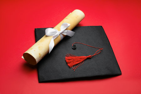 Diploma and graduation hat on red background
