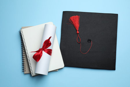 Diploma, graduation hat and notebooks on light blue background, flat layの写真素材
