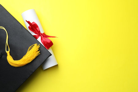 Diploma and graduation hat on yellow background, top view. Space for textの写真素材