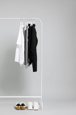 Different clothes hanging on rack and shoes against gray background, space for textの写真素材