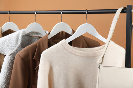 Different clothes and bag hanging on rack against brown background, closeupの写真素材