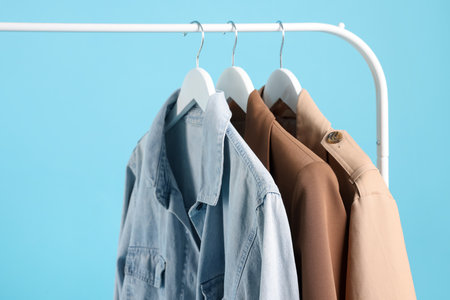 Different clothes hanging on rack against light blue background, closeupの写真素材