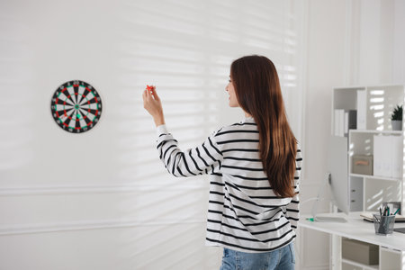 Woman with dart aiming at dartboard indoors, selective focusの写真素材