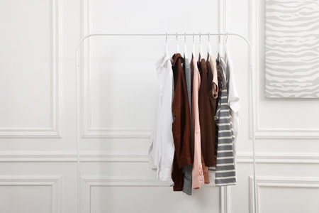 Different women's clothes hanging on rack near white wall indoorsの写真素材