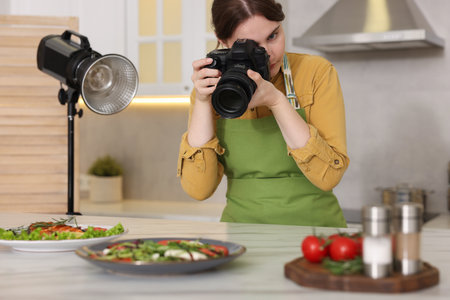 Woman taking picture of meal at table in kitchen. Professional food photographyの写真素材