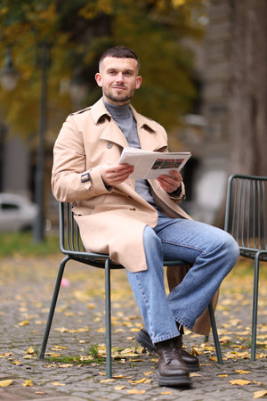 Young man reading newspaper on chair outdoorsの写真素材