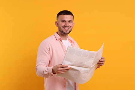 Young man reading newspaper against yellow backgroundの写真素材