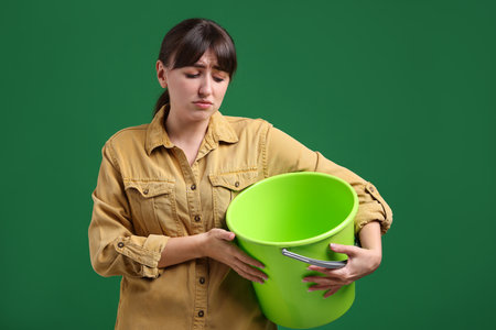 Young woman with bucket suffering from nausea on green backgroundの写真素材