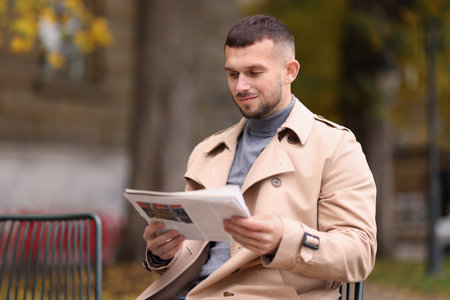 Young man reading newspaper on chair outdoors. Space for textの写真素材