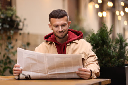 Young man reading newspaper at table in outdoor cafeの写真素材