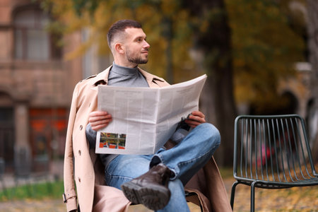 Young man reading newspaper on chair outdoorsの写真素材