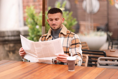 Young man reading newspaper at table in outdoor cafeの写真素材