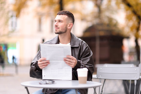 Young man reading newspaper at table in outdoor cafeの写真素材