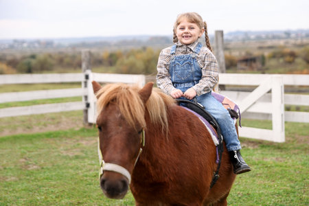 Equine assisted therapy. Little girl riding beautiful pony outdoors. Lovely domesticated petの写真素材