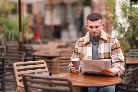 Young man reading newspaper while having coffee at table in outdoor cafe. Space for textの写真素材