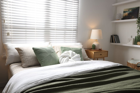 Stylish bedroom with large bed, pillows, houseplant and lamp. Interior design