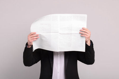 Young man reading newspaper against light gray background