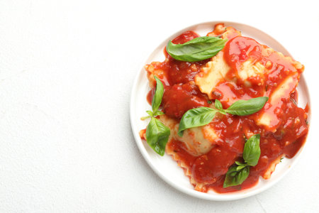 Delicious ravioli with tomato sauce and basil on white textured table, top view. Space for textの写真素材