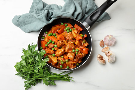 Delicious cooked stew in frying pan, parsley and garlic on white marble table, flat layの写真素材