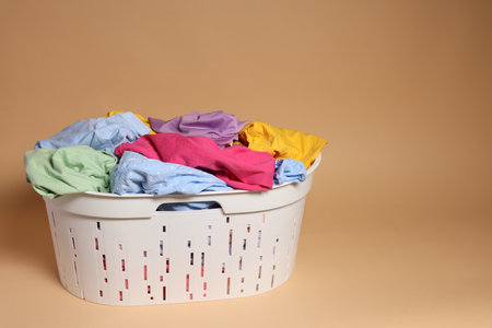 Laundry basket with clothes on light brown background. Space for textの写真素材