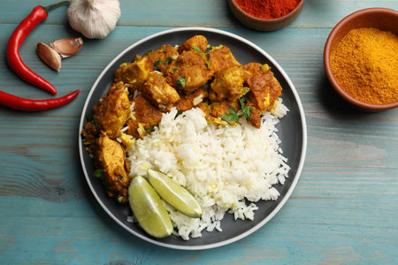 Delicious chicken tikka masala with rice, parsley, lime and spices on light blue wooden table, flat layの写真素材