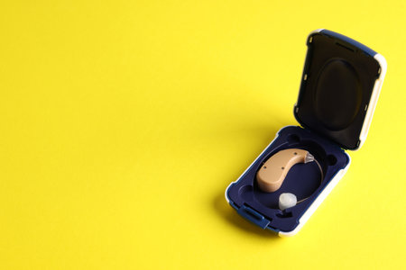 Modern hearing aid in box on yellow background, closeup. Space for textの写真素材