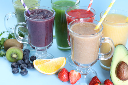Different tasty smoothies in glasses and ingredients on light blue background, closeupの写真素材