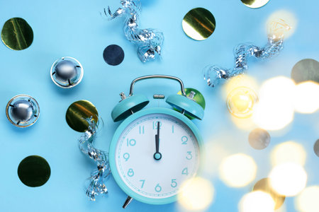 New Year celebration. Alarm clock and festive decor on light blue background, flat lay