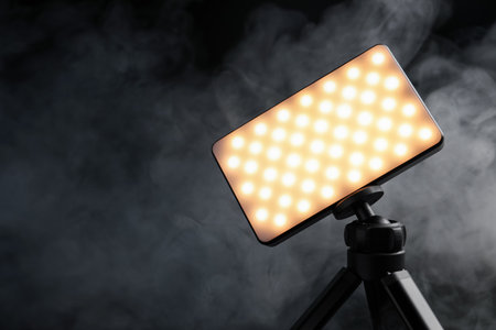 LED lamp on tripod against black background with smoke, closeup. Space for textの写真素材