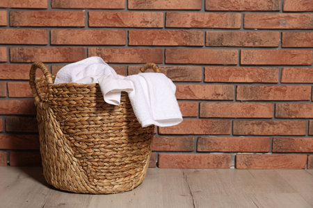 Wicker basket full of laundry on floor near brick wall indoors. Space for textの写真素材