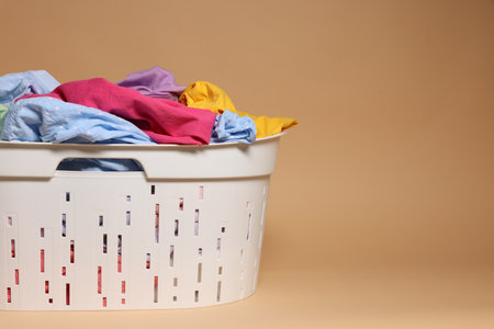 Laundry basket with clothes on light brown background, closeup. Space for textの写真素材