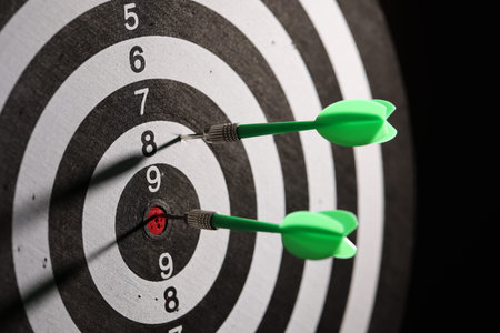 Dartboard with darts on black background, closeup