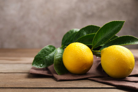 Wet lemons with green leaves and brown napkin on wooden table against gray background, closeup. Space for textの写真素材