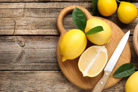 Whole, cut lemons with green leaves and knife on wooden table, flat lay. Space for textの写真素材