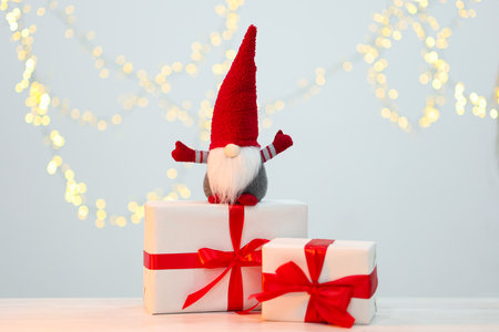 Christmas gnome and gift boxes on white wooden table against background with blurred lights. Bokeh effectの写真素材